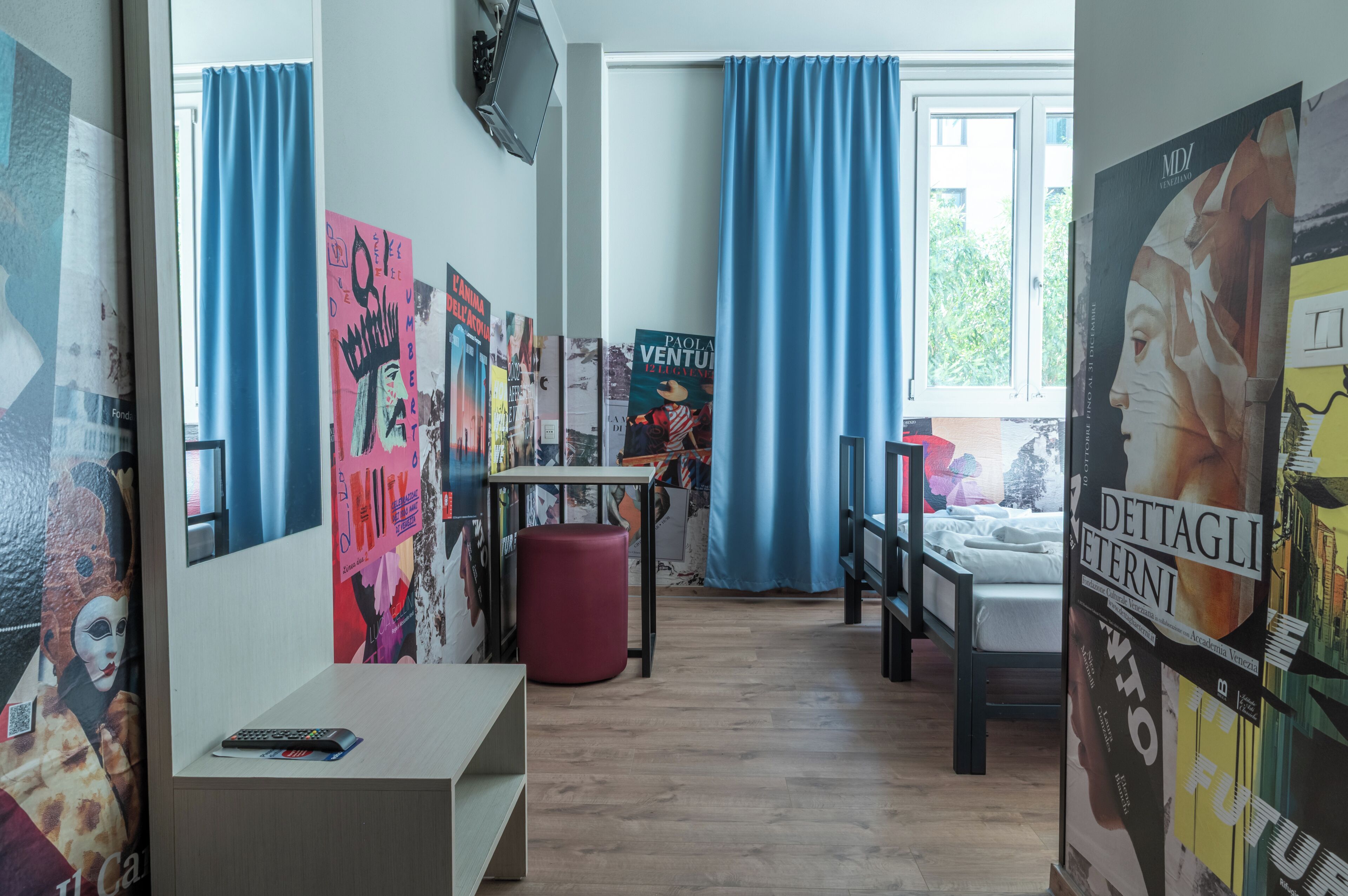 A room with a bed, a desk, and a chair. There are posters on the walls and a window with curtains.