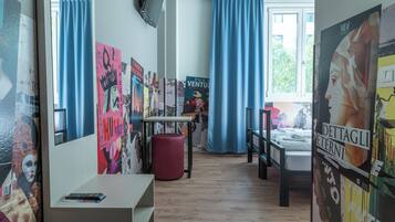 A room with a bed, a desk, and a chair. There are posters on the walls and a window with curtains.