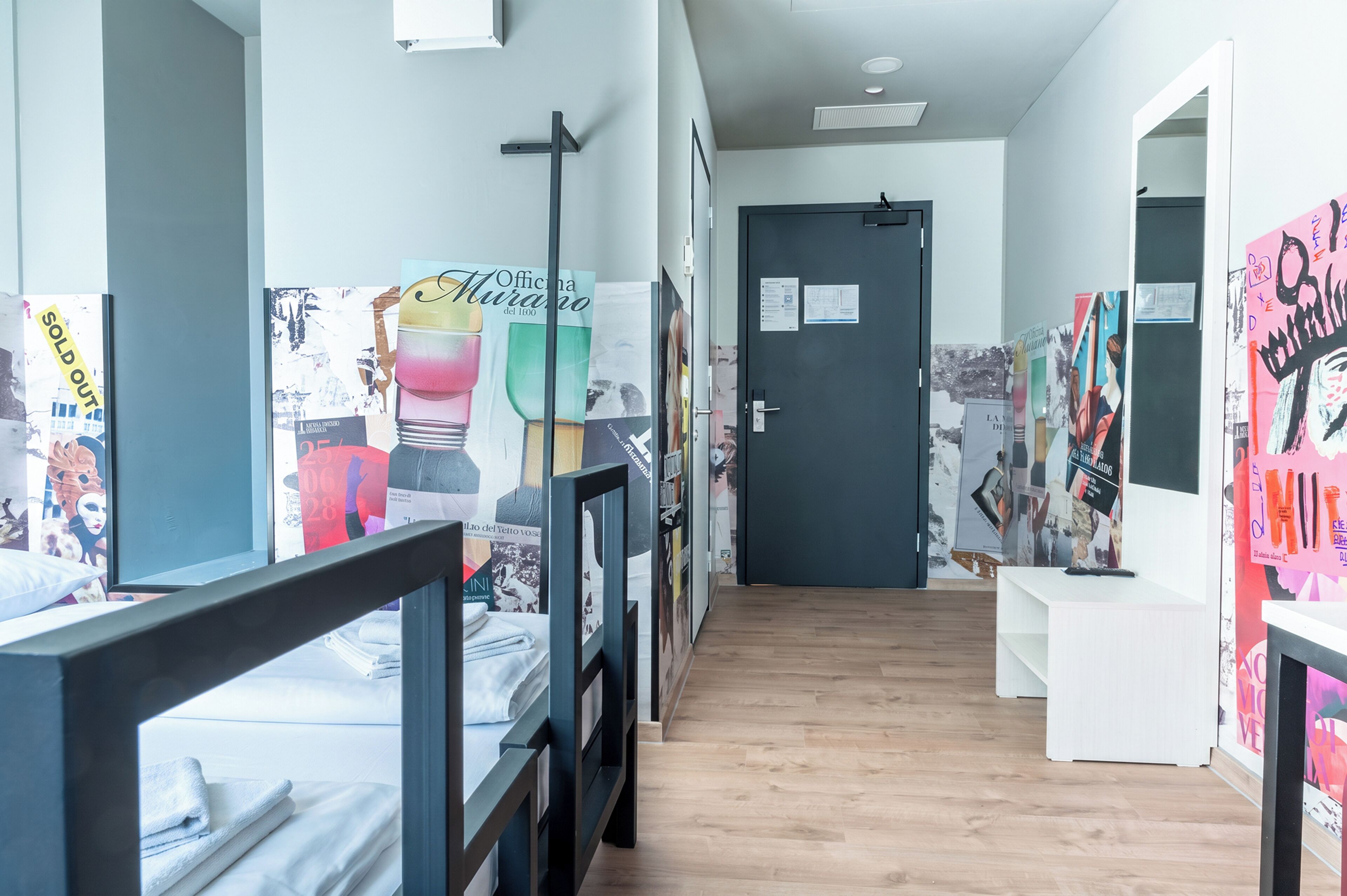 Un couloir avec des lits superposés, une porte et des murs décorés de divers affiches et œuvres d’art.