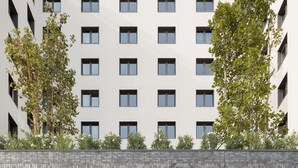 Een modern gebouw met een betegelde gevel, grote ramen en een overdekte entree met zitplaatsen.