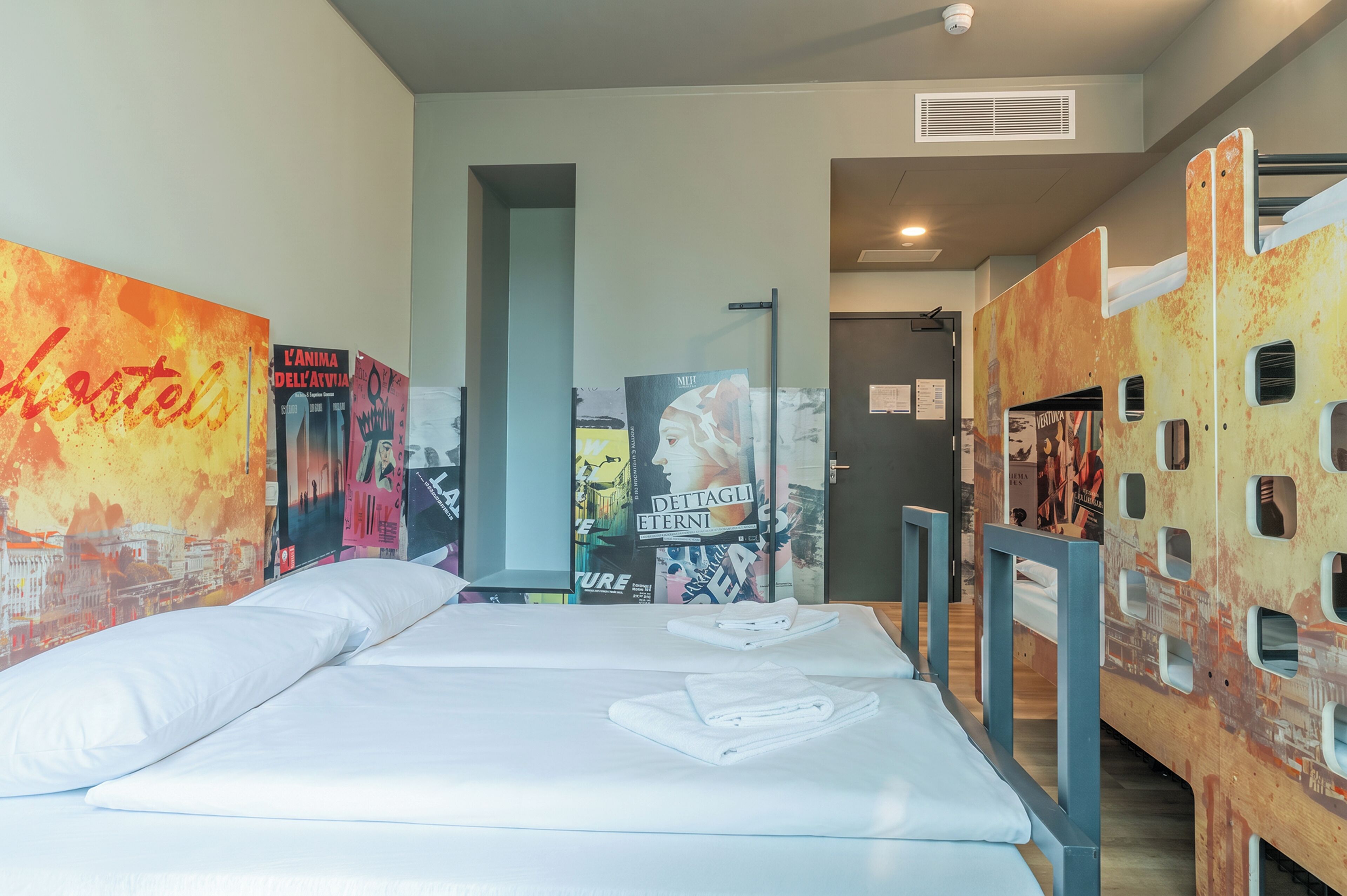 A hotel room with a bed, a window, and a wall with posters.