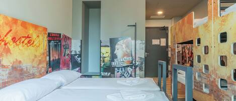 A hotel room with a bed, a window, and a wall with posters.