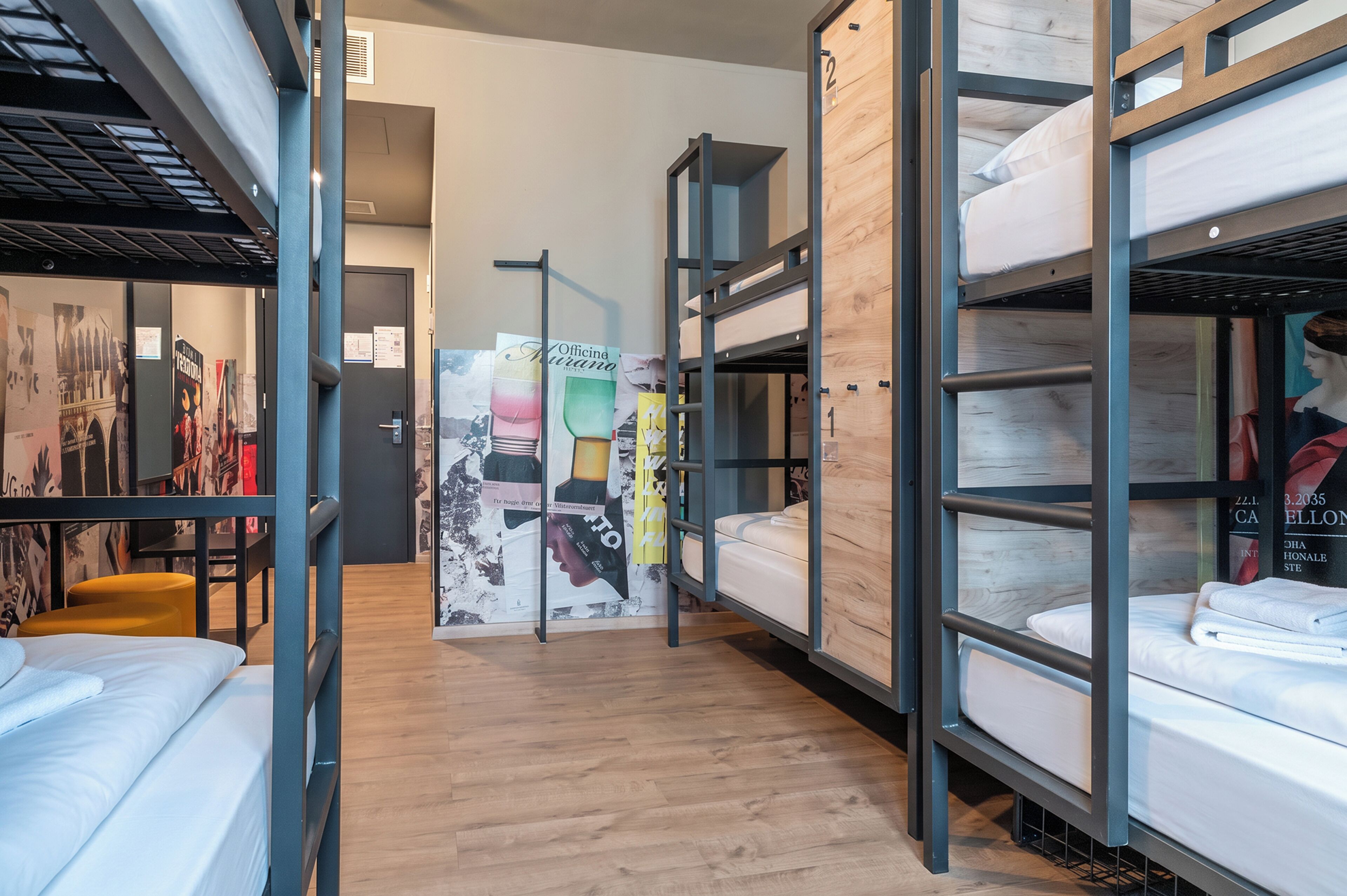Habitación de albergue con camas literas, piso de madera y una pared decorada con carteles y un mapa.
