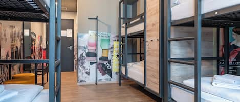 A hostel room with bunk beds, a wooden floor, and a wall with various posters and a map.