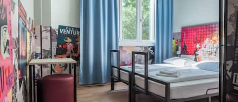 A bedroom with a bed, a small table, a red ottoman, and a window with curtains.