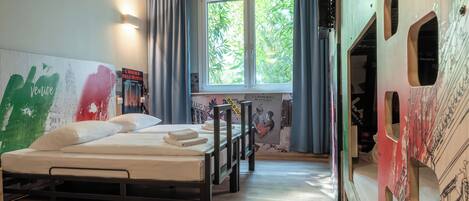 Una habitación con cama, ventana con cortinas y un muro con carteles.