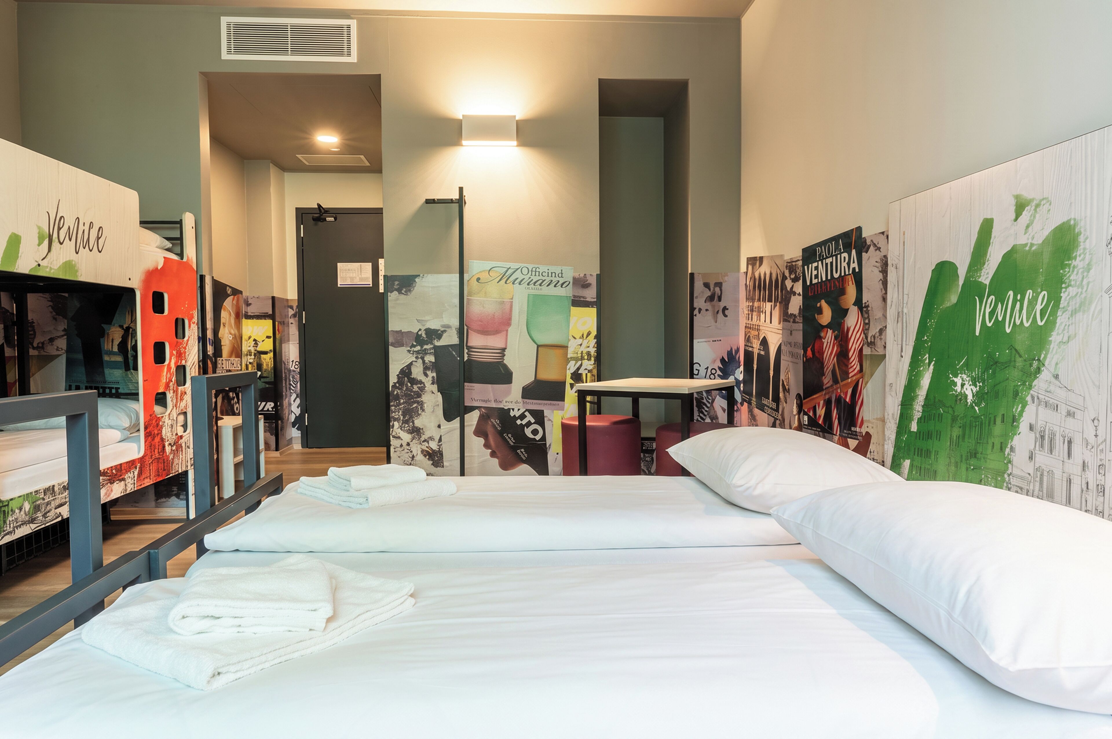A hotel room with a bed, towels, a desk, and artwork on the walls.