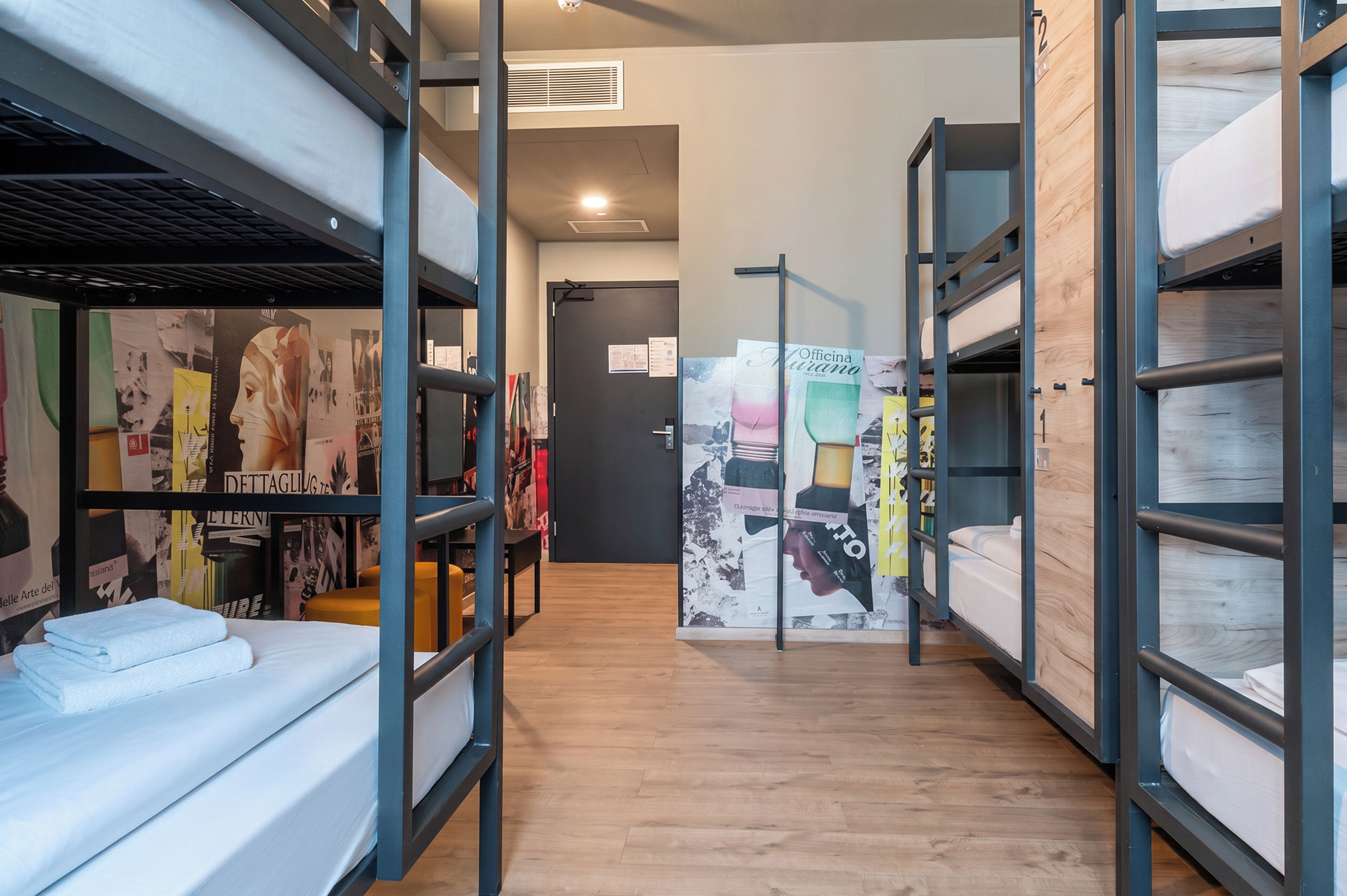 Una camera d'ostello con letti a castello, pavimento in legno e una parete decorata con diversi poster.