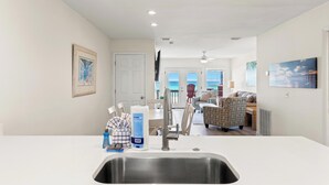 A modern kitchen with a stainless steel sink, a dining area with a table and chairs, and a view of the ocean through large windows. - Premier Townhomes by Panhandle Getaways (Panama City Beach)