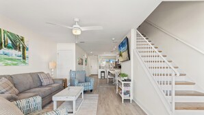 A modern living room with a sofa, armchairs, a coffee table, a staircase, and a kitchen area in the background. - Premier Townhomes by Panhandle Getaways (Panama City Beach)
