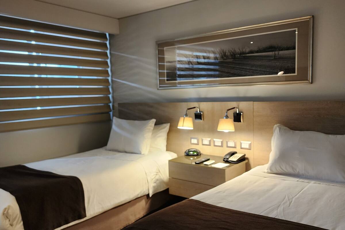 A hotel room with two beds, a nightstand with a phone and lamp, and a framed picture on the wall.