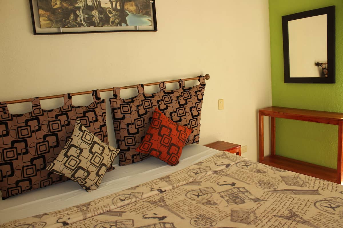 A bed with patterned pillows, a framed picture on the wall, and a green wall.