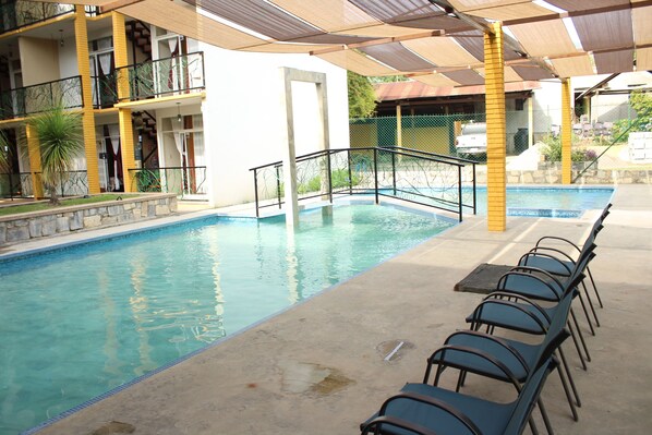 A swimming pool with a sunshade, a stone wall, and a row of chairs. - Hotel Cascada Huasteca (Tanchachin)
