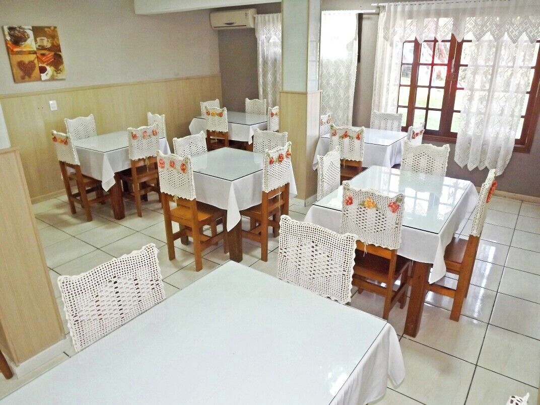 Un espace repas comprenant plusieurs tables et chaises, chacune recouverte d’une nappe blanche et agrémentée de housses de chaise en crochet.