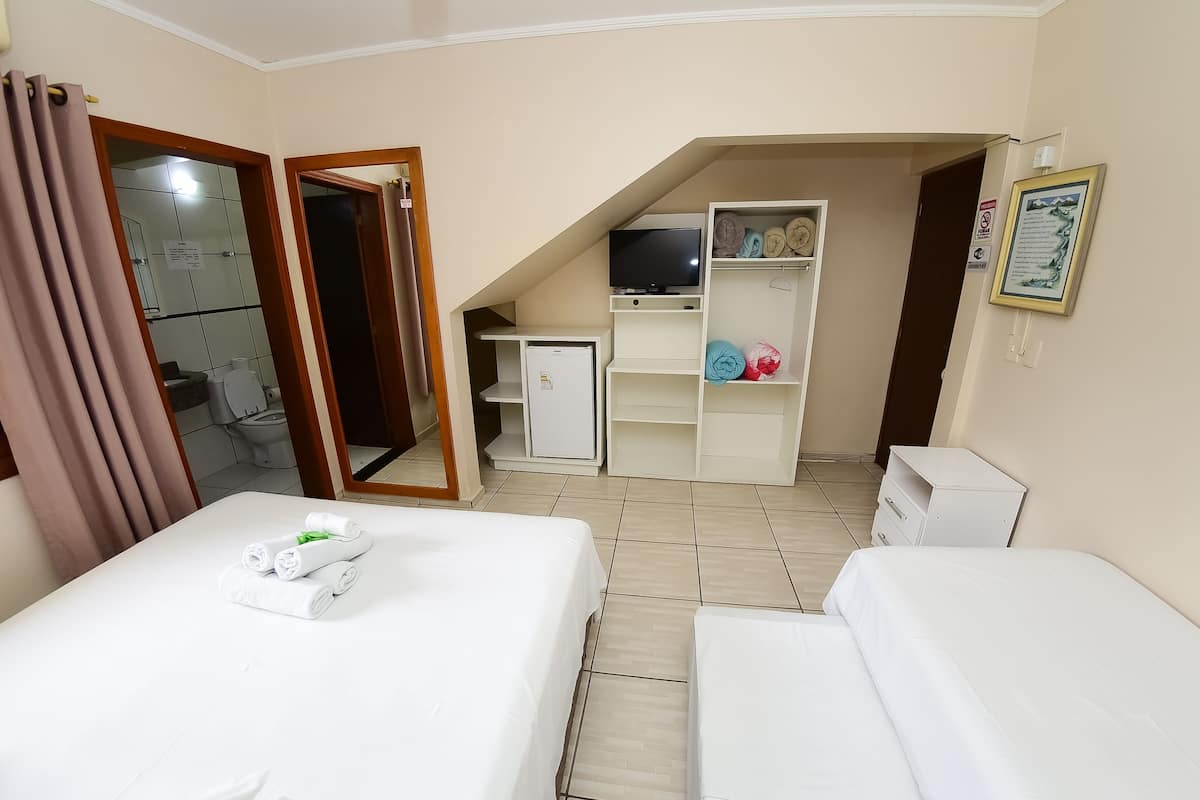 A hotel room with two beds, a TV, a small desk, and a storage unit.