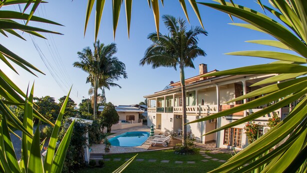 Una casa con piscina, rodeada de palmeras y un césped cuidado.