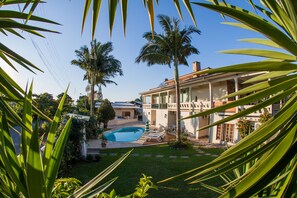 Una casa con piscina, rodeada de palmeras y un césped cuidado.