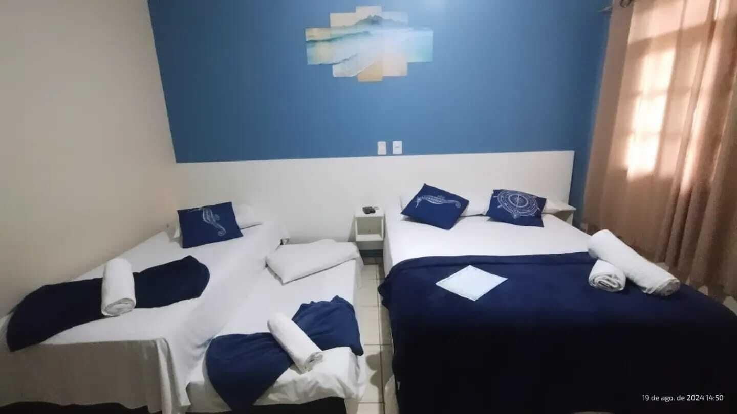 Une chambre d’hôtel avec deux lits, chacun agrémenté de draps et d’oreillers bleus, une petite table de chevet et une œuvre d’art accrochée au mur.