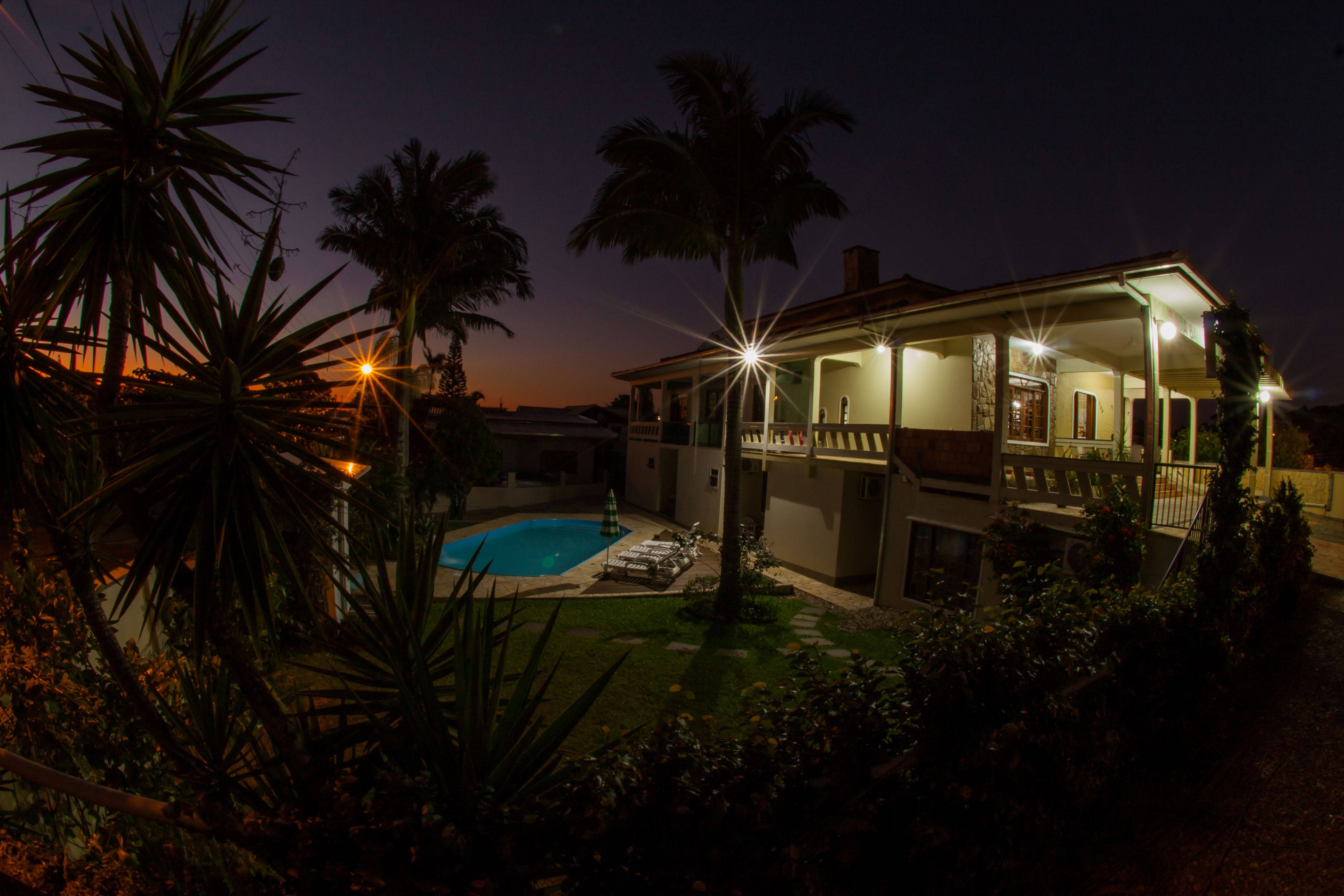 Une maison avec une piscine, entourée de palmiers et dotée d’un porche bien éclairé.