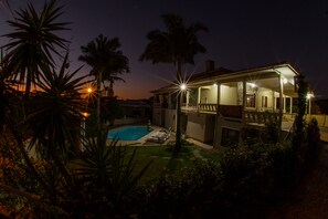Una casa con piscina, rodeada de palmeras y un porche bien iluminado.