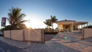 Entrada de hotel con un camino de piedra, palmeras y cielo despejado.