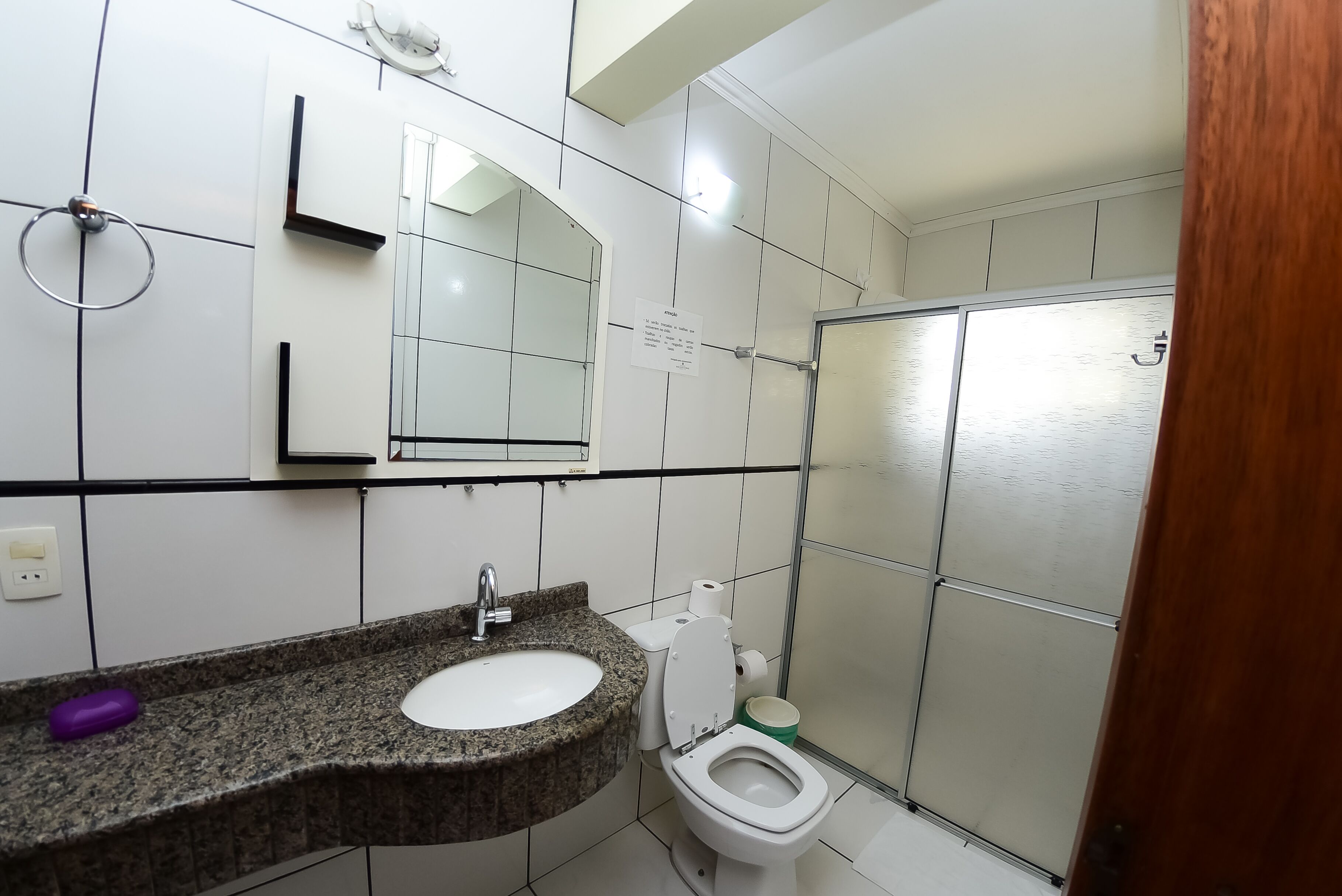 Een badkamer met een wastafel met granieten blad, een spiegel, een toilet en een douchehoek.
