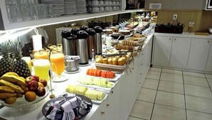 Un bufé con diversos alimentos y bebidas, incluyendo frutas, pastelería y una estación de café.