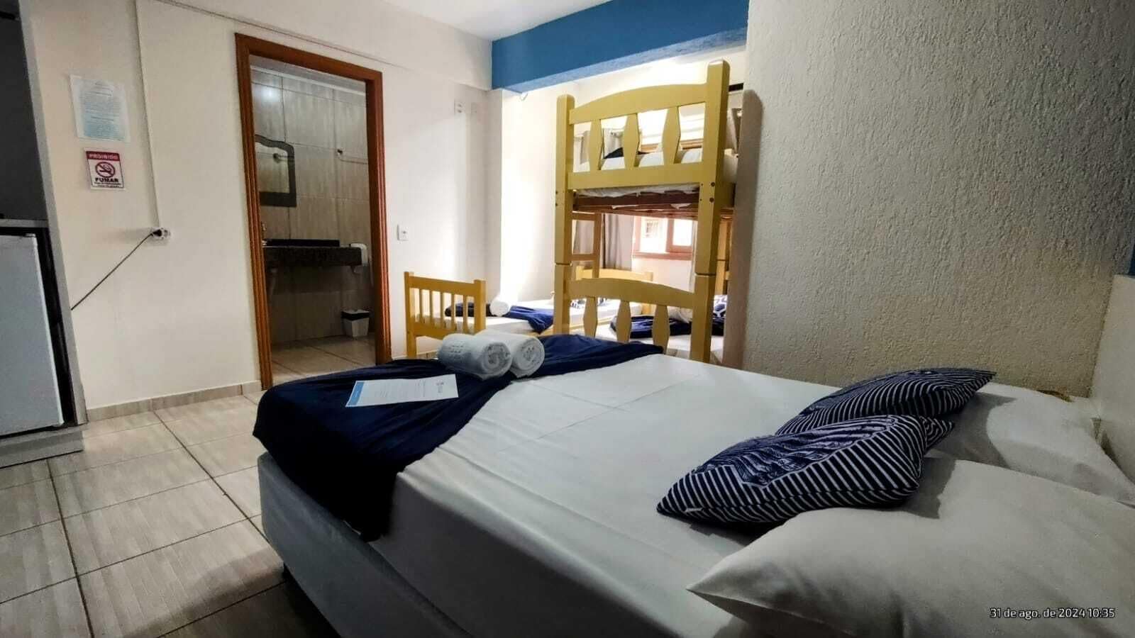 A hotel room with a bed, a wooden bunk bed, a chair, and a small table.