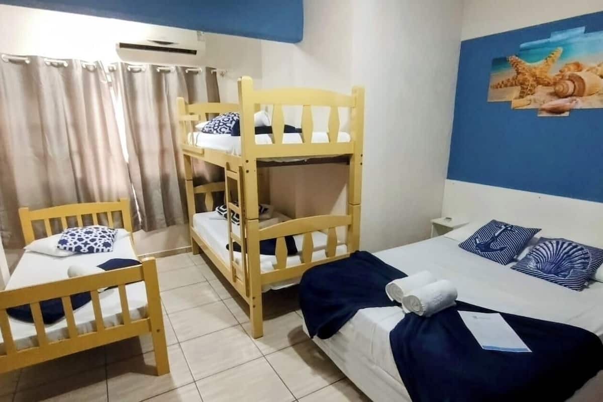 A room with a bunk bed, a single bed, a chair, and a wall with a seashell mural.