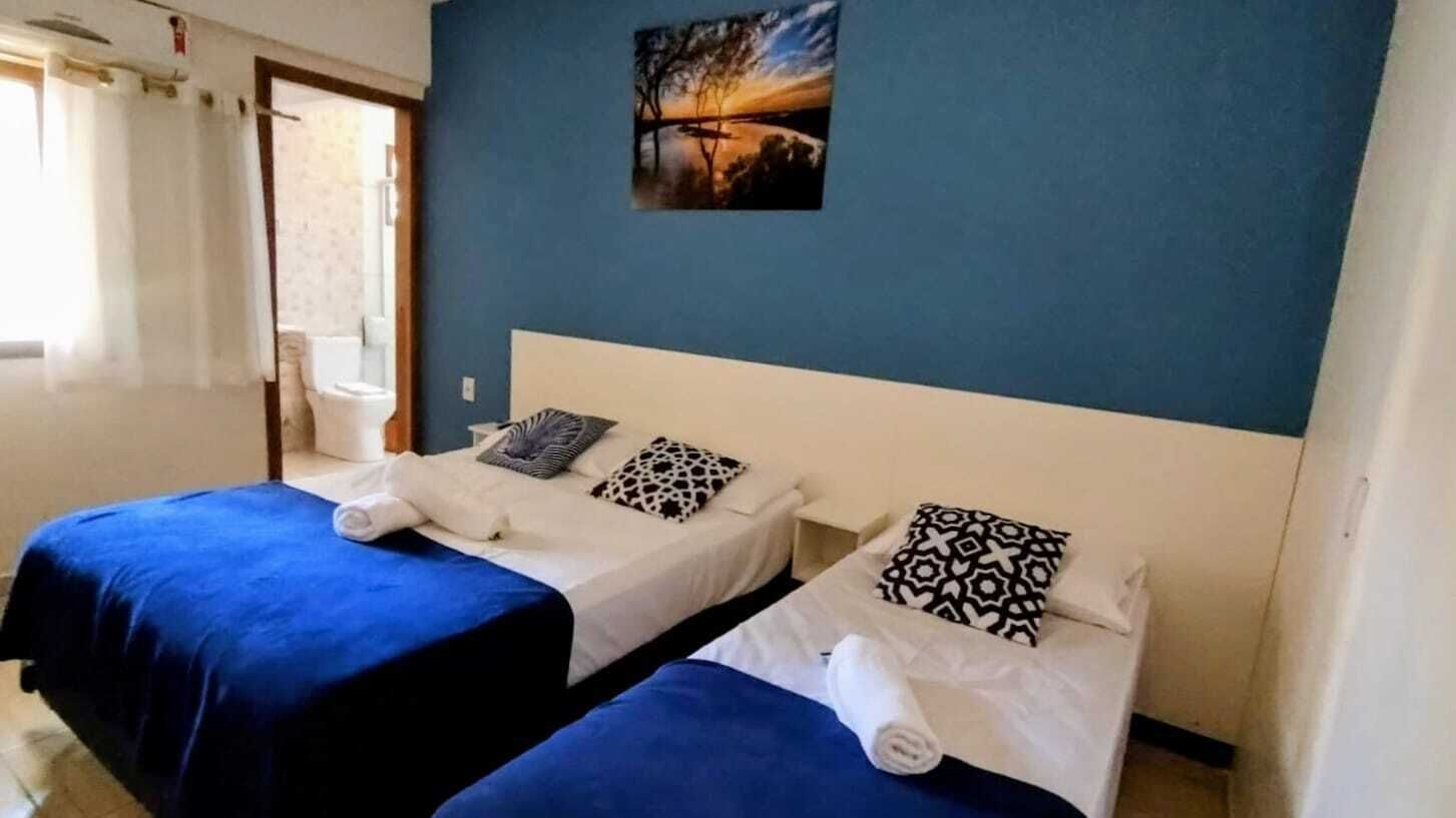 Une chambre avec deux lits, chacun recouvert d’une courtepointe bleue et de draps blancs, un tableau au mur et une fenêtre avec des rideaux.