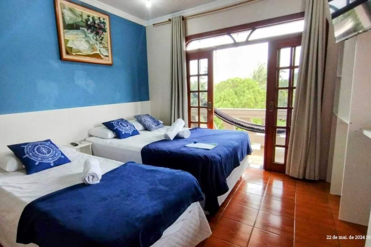 A hotel room with two beds, a painting on the wall, and a view through a glass door.