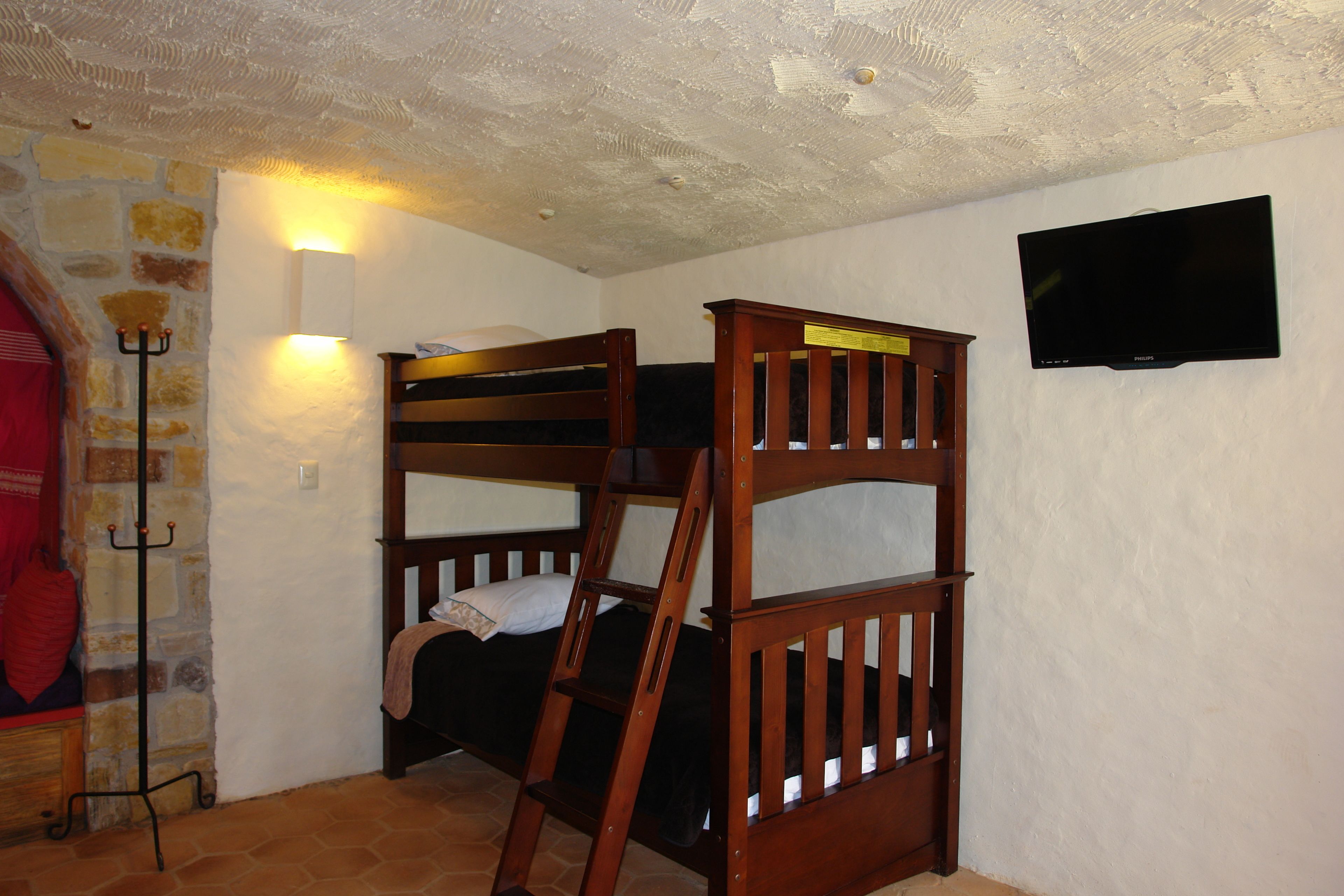 Una cama individual superpuesta con una escalera, un televisor montado en la pared y una pared de piedra con una cortina roja.
