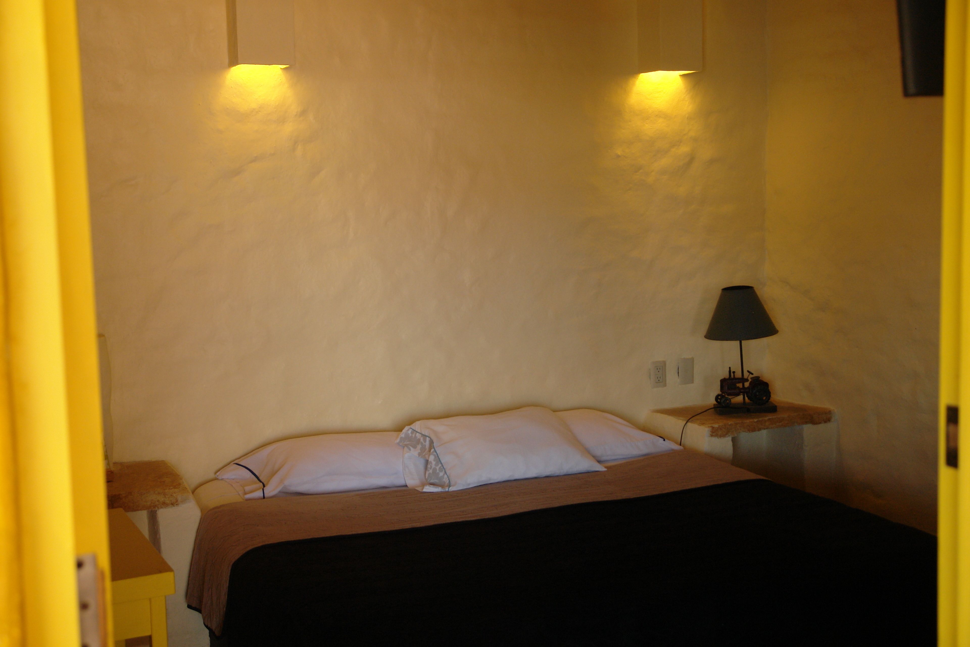 A bedroom with a bed, a nightstand, a lamp, and a wall-mounted light fixture.