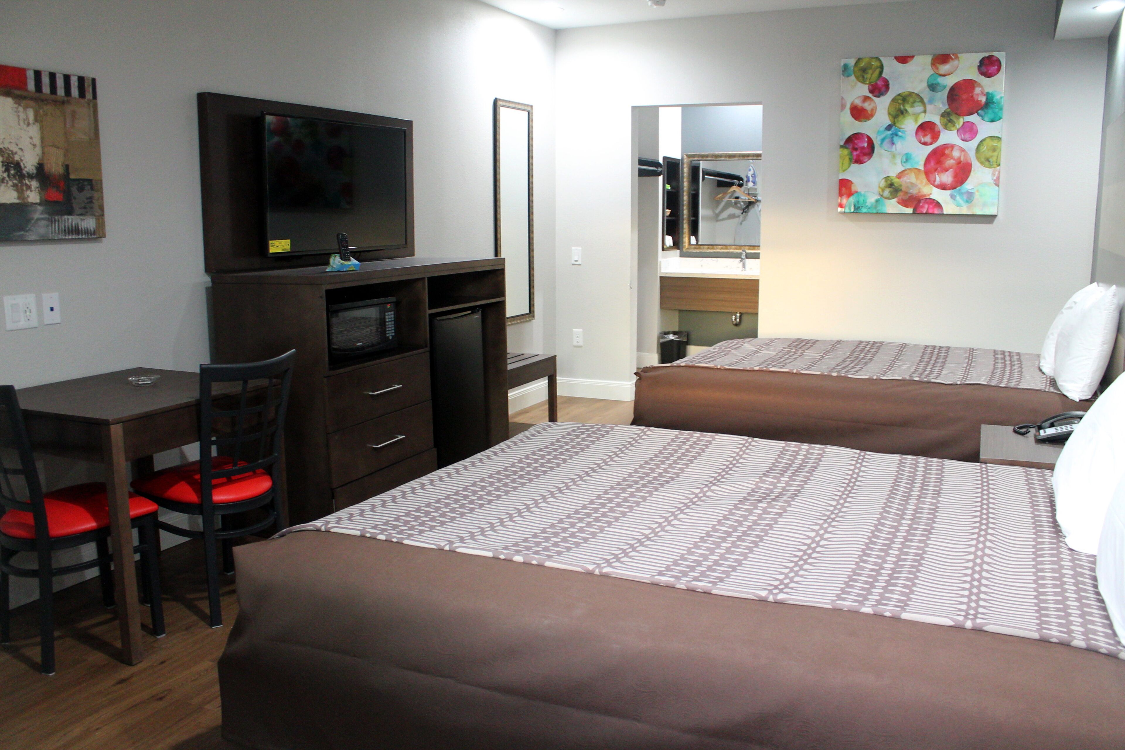 A hotel room with two beds, a desk with a chair, a television, and a mirror.