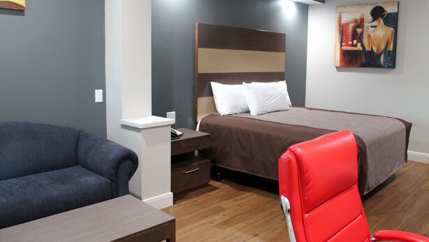 A hotel room with a bed, a red chair, a sofa, a nightstand, and a painting on the wall. - Grand Villa Inn & Suites Chinatown (Houston)