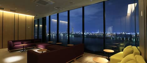 A modern hotel lobby with a large seating area, a city view through large windows, and a clean, contemporary design.