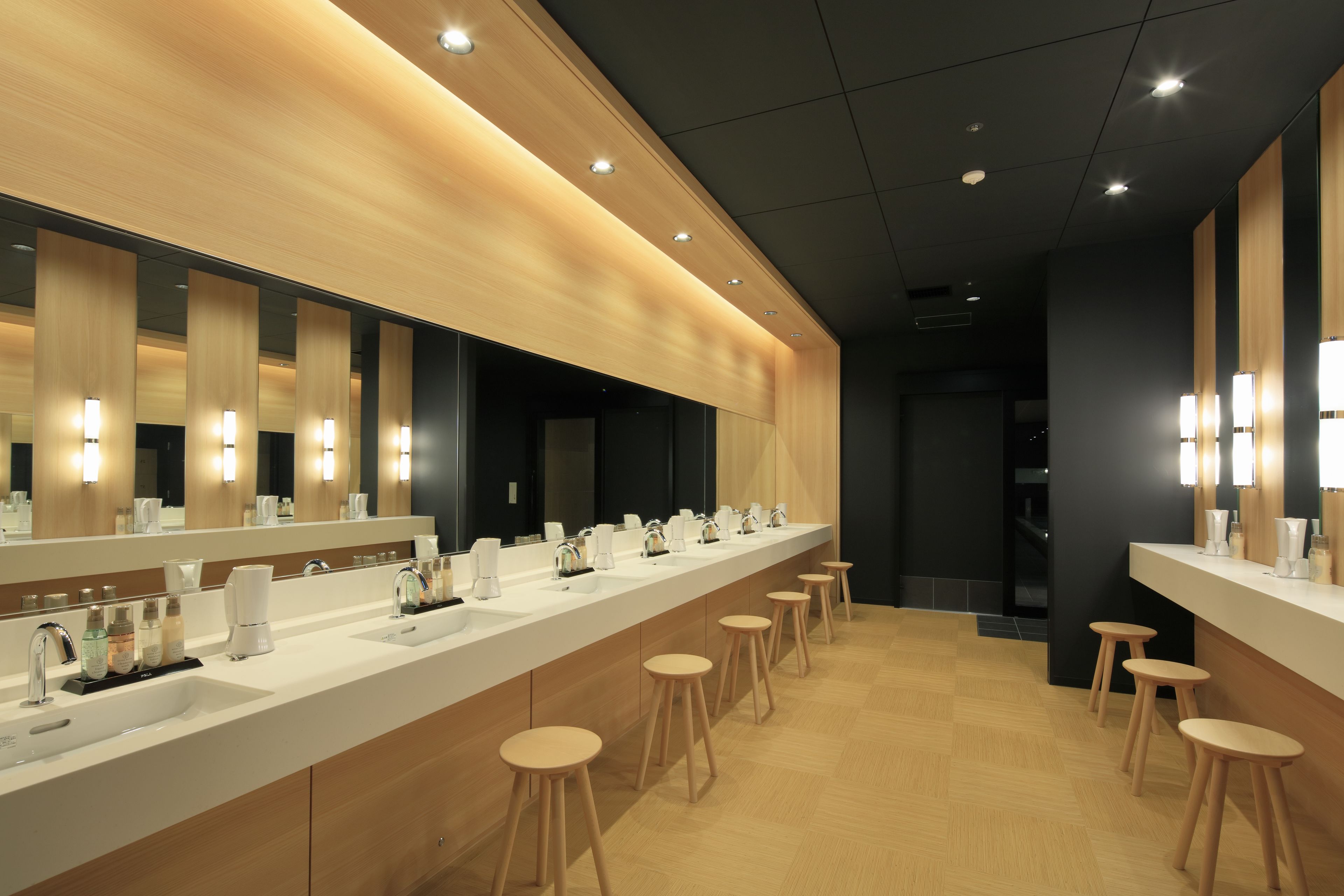 A modern bathroom with a long vanity, multiple sinks, and wooden stools.