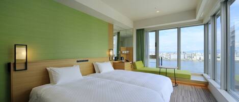A hotel room with two large beds, a green wall, a large window with a city view, and a small table.