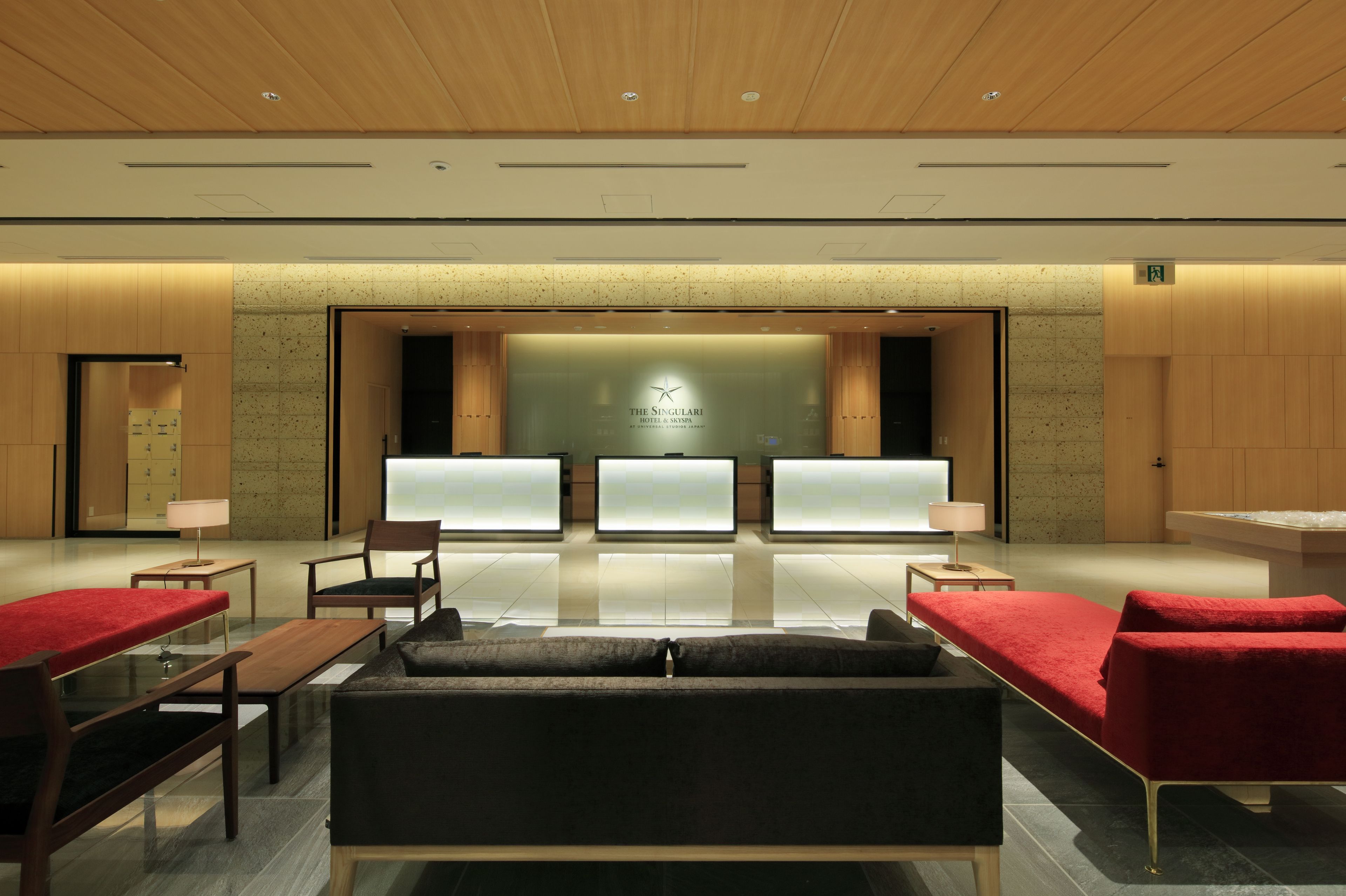 A modern hotel lobby with a reception desk, seating area, and a large wall with a logo.