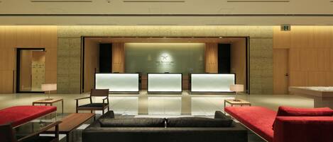 A modern hotel lobby with a reception desk, seating area, and a large wall with a logo.