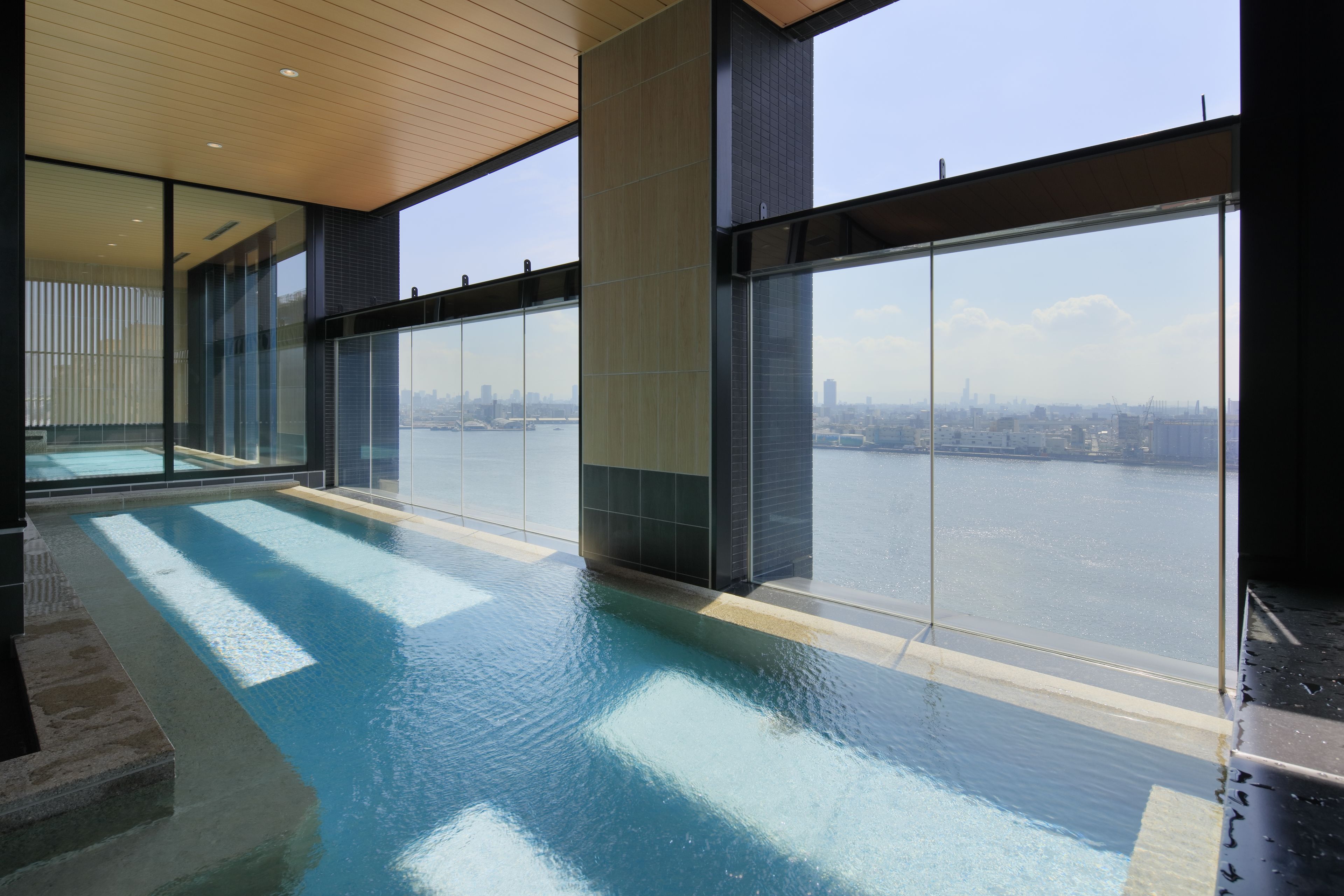 An indoor swimming pool with large windows offering a view of a city skyline and a body of water.