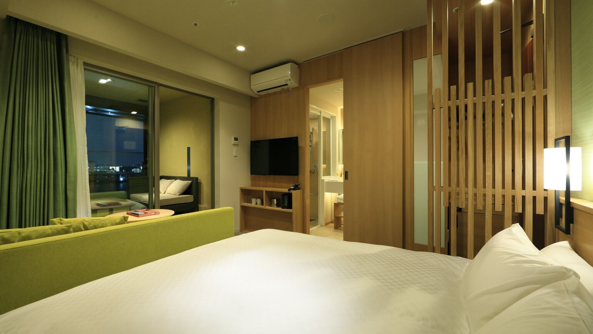A hotel room with a bed, a TV, a sofa, a desk, and a shower area.