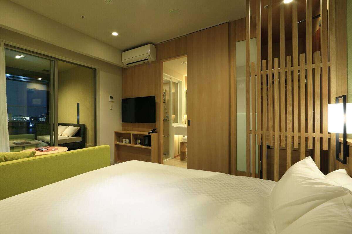 A hotel room with a bed, a TV, a sofa, a desk, and a shower area.