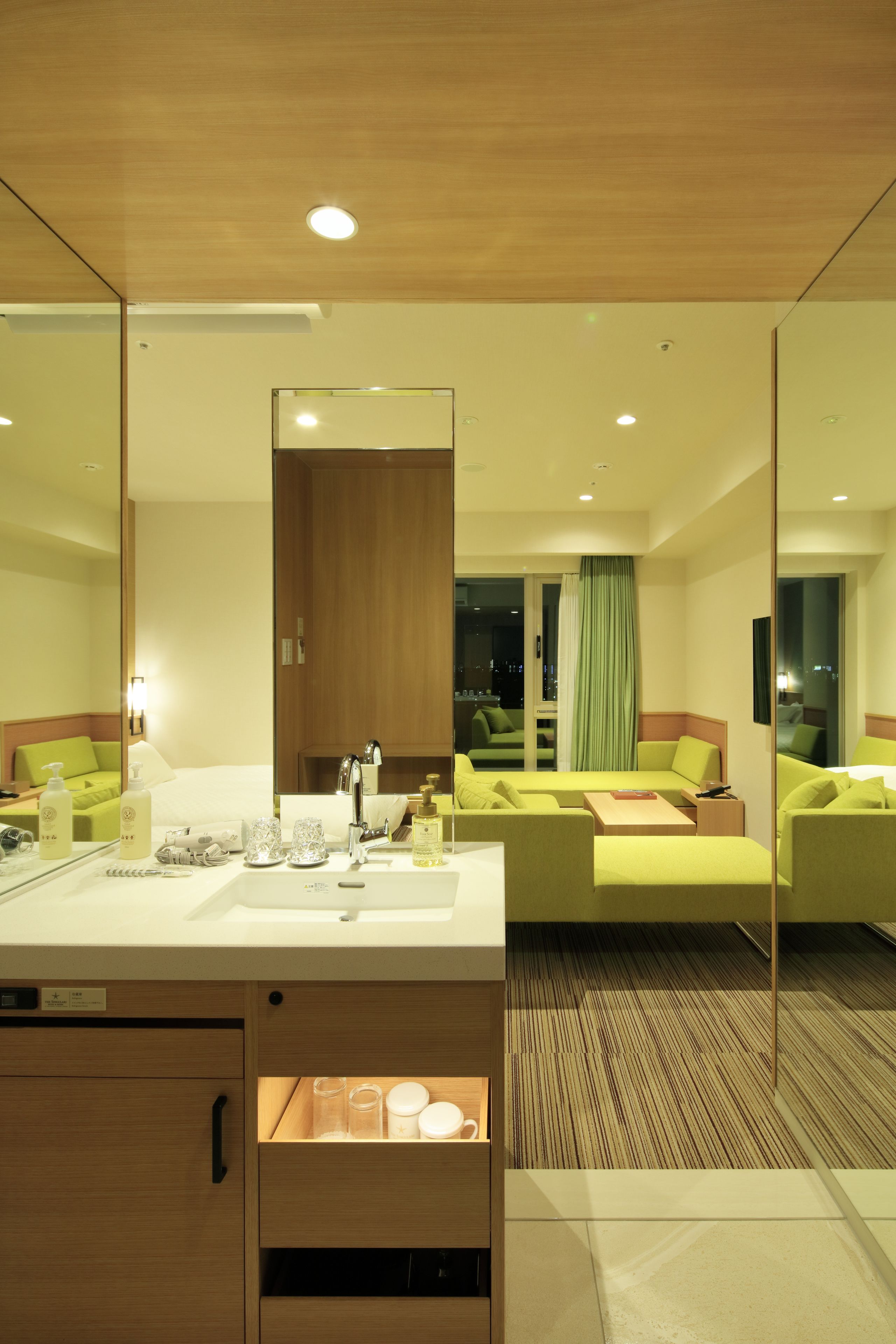 A modern hotel room with a large mirror, a wooden ceiling, a green sofa, and a white sink.