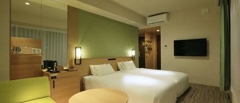 A hotel room with a large bed, a small table, a sofa, a TV, a coffee machine, and a mirror.