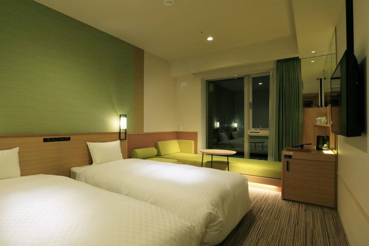 A hotel room with two beds, a sofa, a small table, a TV, and a view of the city at night.