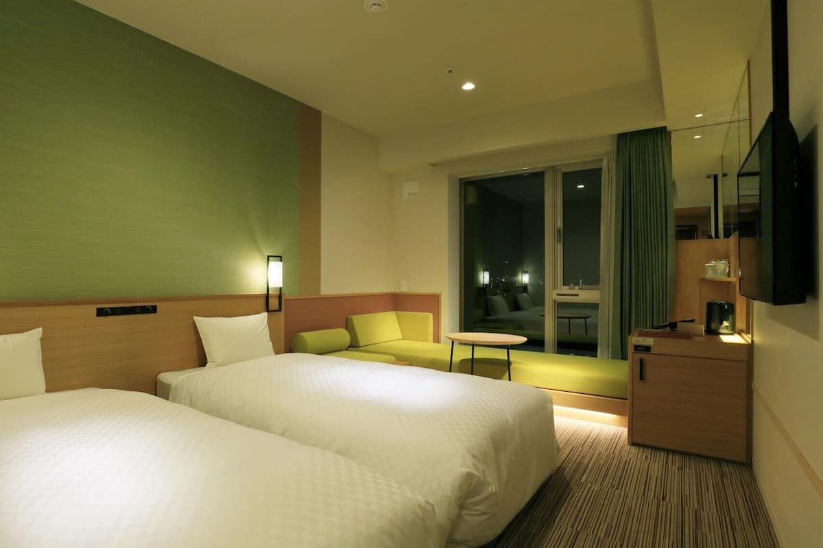 A hotel room with two beds, a sofa, a small table, a TV, and a view of the city at night.