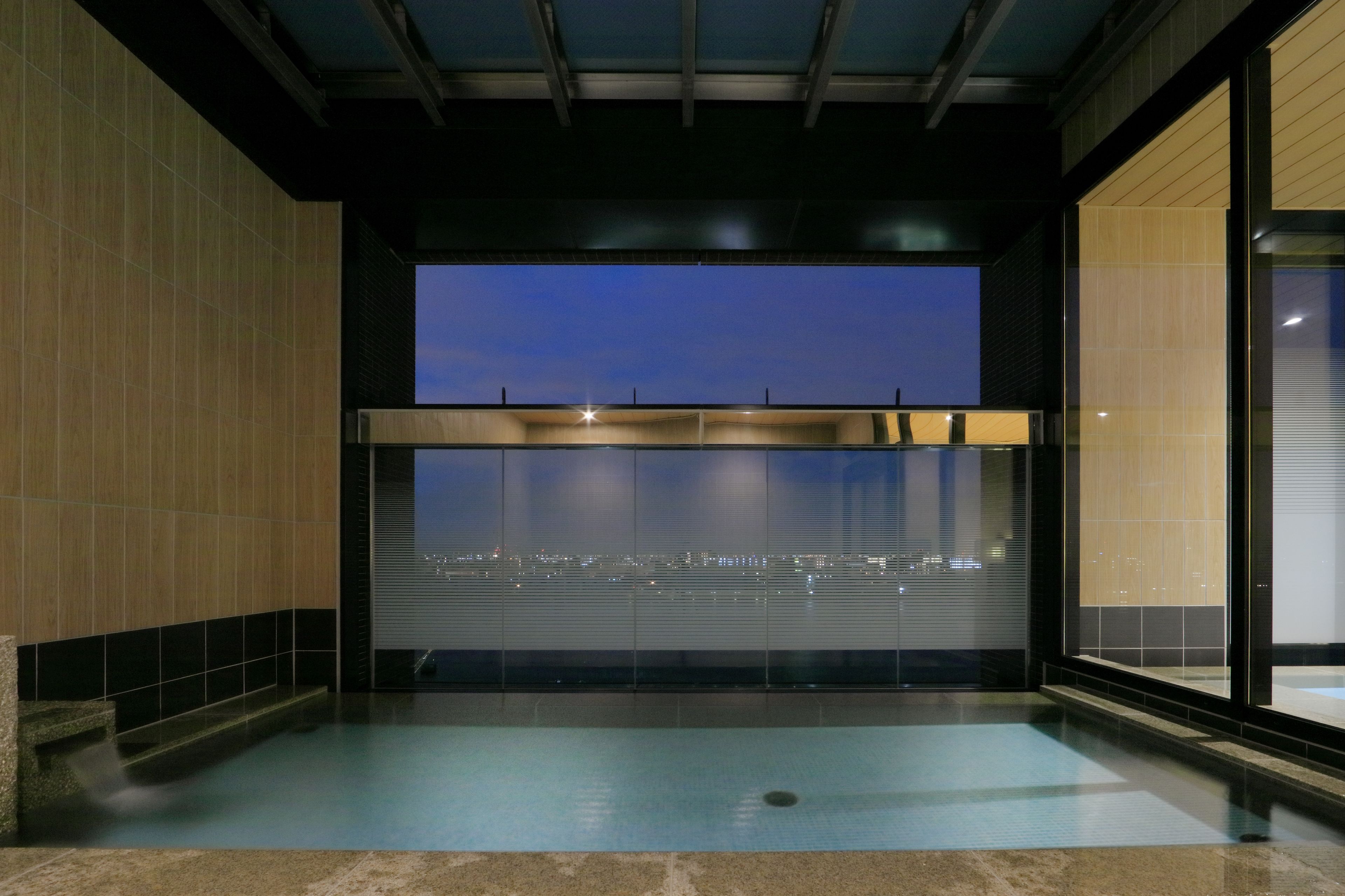 A modern indoor swimming pool with a city view, a glass wall, and a ceiling with a grid pattern.