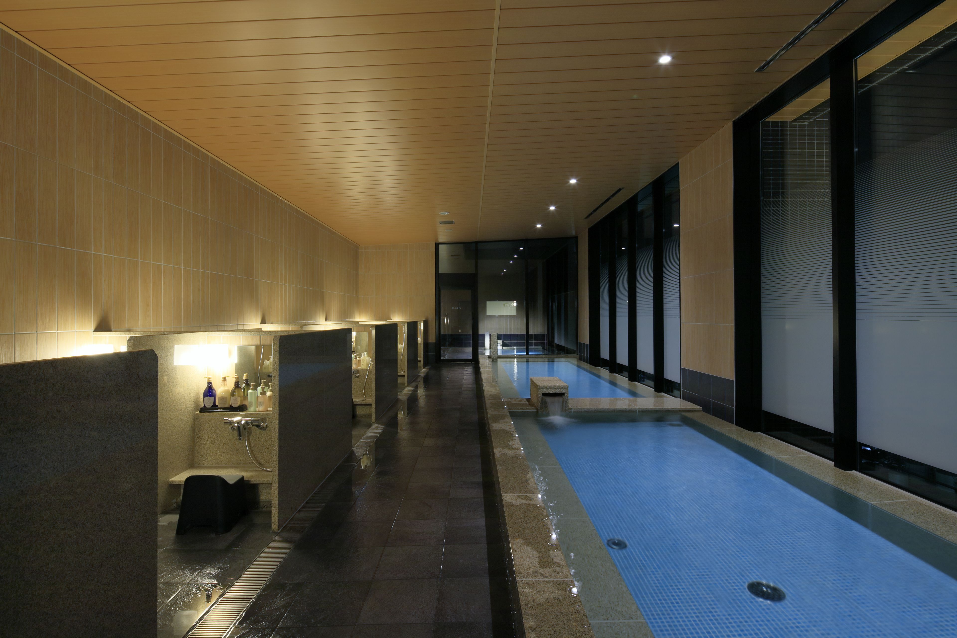 A corridor with a blue pool area, a seating bench, and a small seating area with a bench and table.