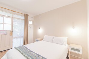 A hotel room with a bed, bedside tables, a window with curtains, and a door. - Warburton Lodge (Warburton)